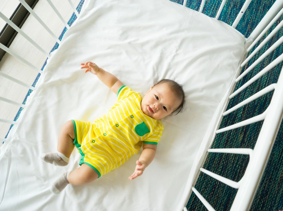 A baby is laying in a crib on its side.